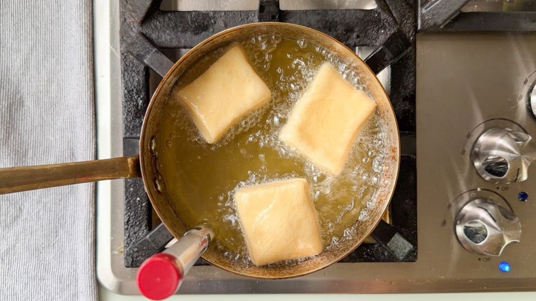 Beignet dough cooking in hot oil on stovetop