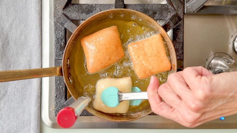 Turning beignets in hot oil with tongs
