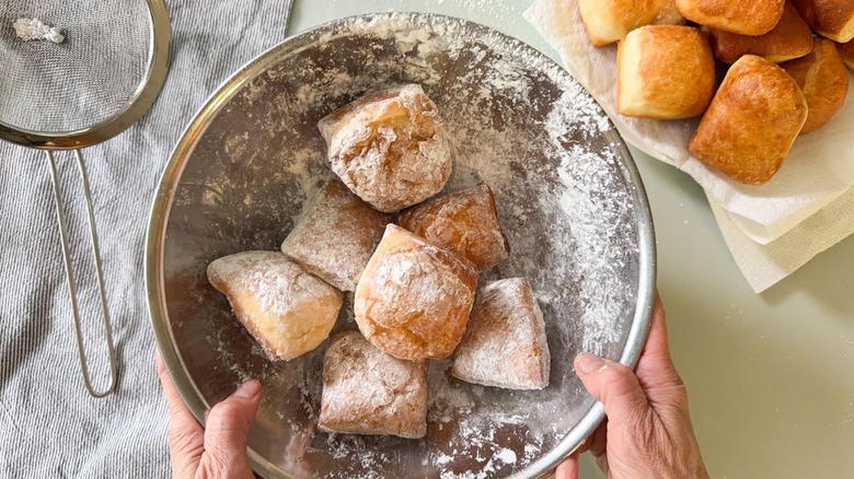 Tossing beignets in confectioner's sugar in stainless steel bowl