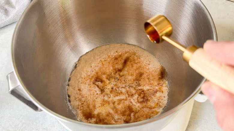Adding vanilla extract to beignet dough in stand mixer bowl with teaspoon measure
