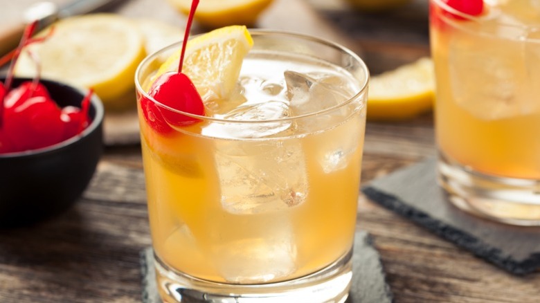 Light-colored whiskey sours garnished with lemon wedges and cherries.