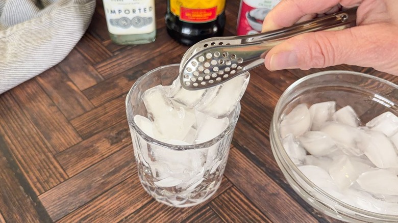 Using tongs to fill a rocks glass with ice