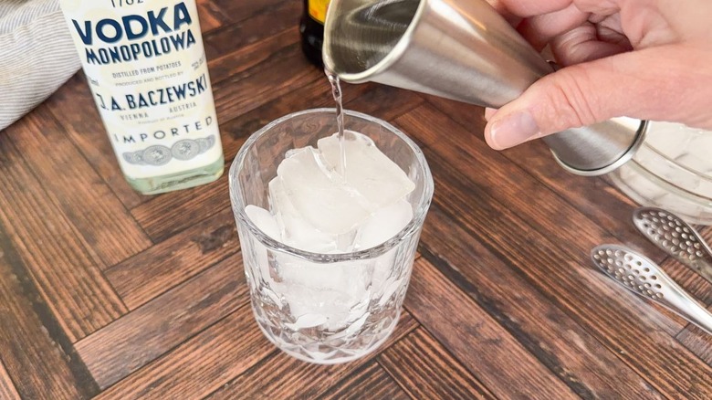 Pouring vodka over ice in rocks glass