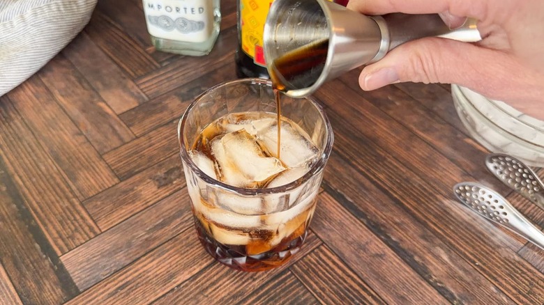 Pouring Kahlua over vodka and ice in rocks glass