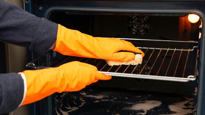 A pair of hands wearing rubber gloves, wiping the dirt on an oven rack.