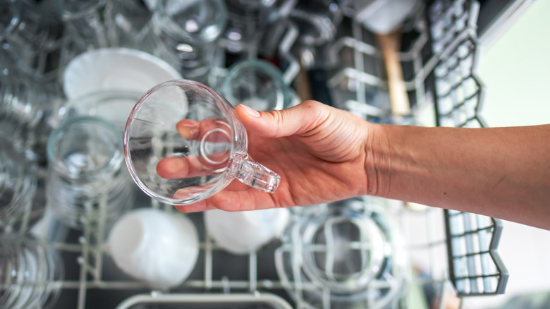 A hand removing clean glasses from the top rack of a dishwasher.