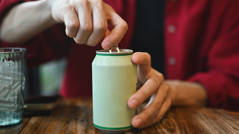 A person's hands open a nondescript soda can.