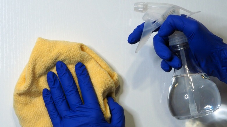 Gloved hands cleaning with a bottle of white vinegar and a yellow rag.