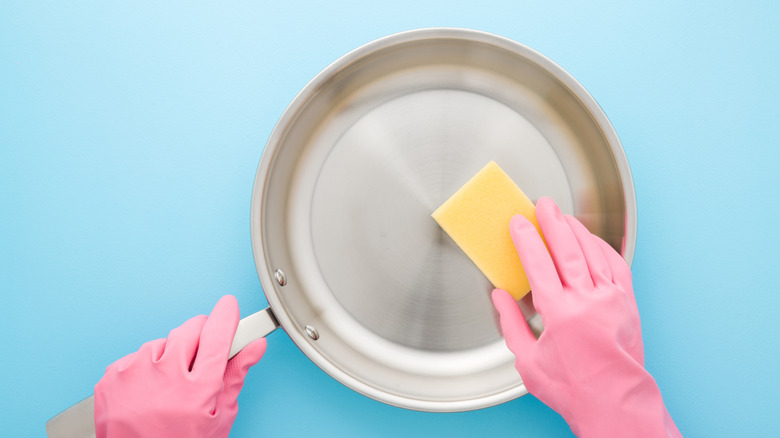 hands with rubber gloves wiping a stainless steel pan with a sponge