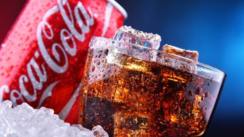 A Coca Cola glass and can on a blue background.