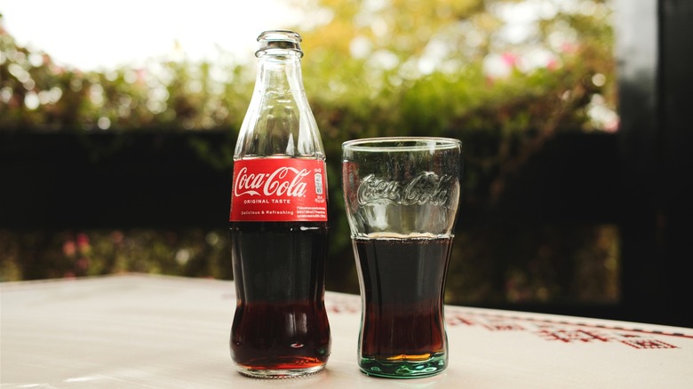 A bottle of Coca-Cola next to a glass of Coca-Cola on a table