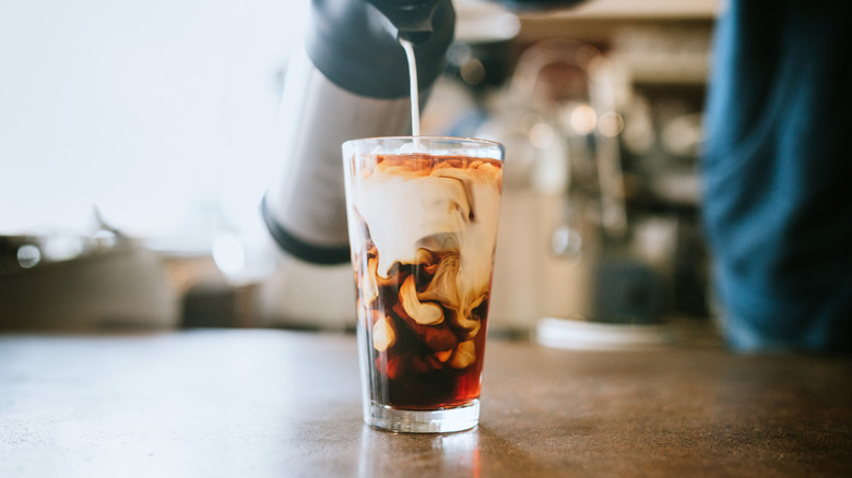 Creamer being poured into a glass of iced coffee