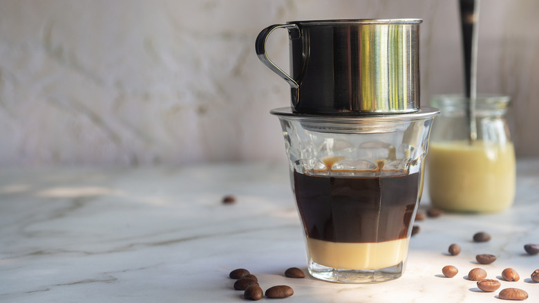 A glass of cà phê sữa đá on a counter with coffee beans