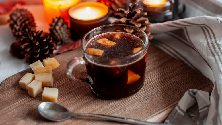 A glass mug of kaffeost on a cutting board with pieces of cheese