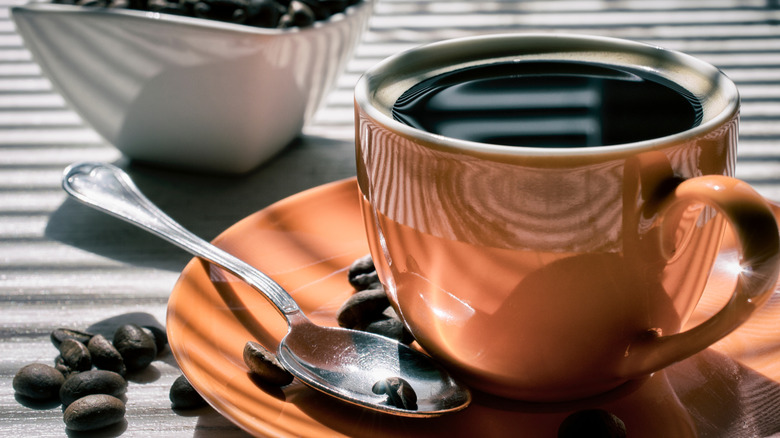 A cup of kahawa chungu coffee on a saucer with a spoon and coffee beans