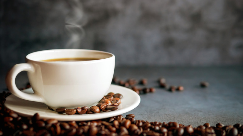 A freshly brewed cup of coffee on a saucer with coffee beans scattered around it