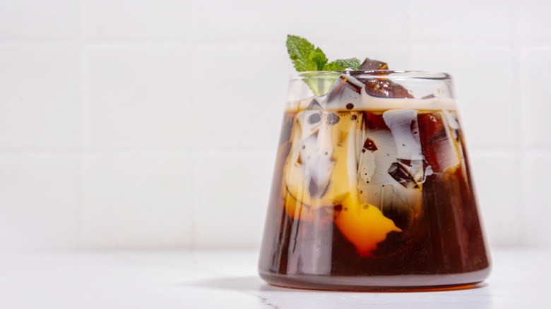 Coffee jelly served in a conical glass over coffee, with a splash of milk, topped with a sprig of mint.