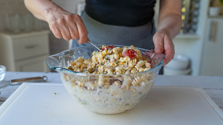A person's hands are seen mixing a bowl of pasta salad