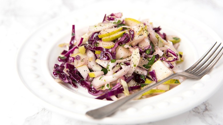 Sliced purple cabbage and chopped pear salad on a white plate with a metal fork