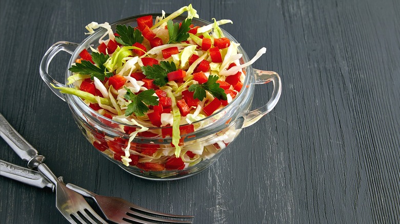 Coleslaw with chopped red pepper and Italian parsley in a glass bowl with handles on a gray surface