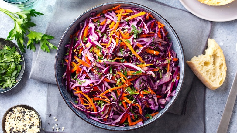 Top-down view of mayonnaise-free coleslaw with purple cabbage, carrot, and green herbs in a gray bowl