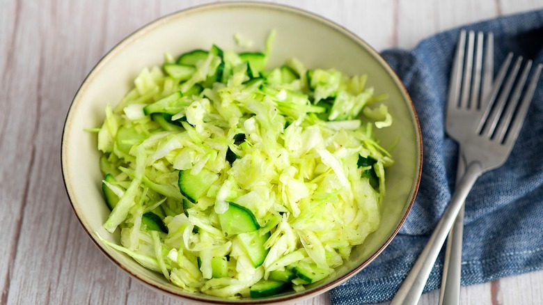 Shredded cabbage and chopped cucumber salad in a shallow bowl next to two metal forks