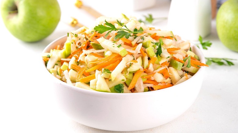 Coleslaw made with shredded carrots, matchstick apples, and fresh parsley in a white bowl
