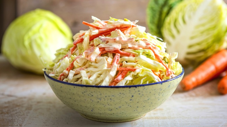 Creamy coleslaw made of shredded carrots and green cabbage in a blue-speckled bowl