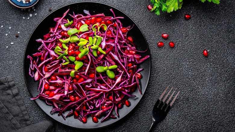 Shredded purple cabbage, pomegranate arils, and small green leaves on a black plate