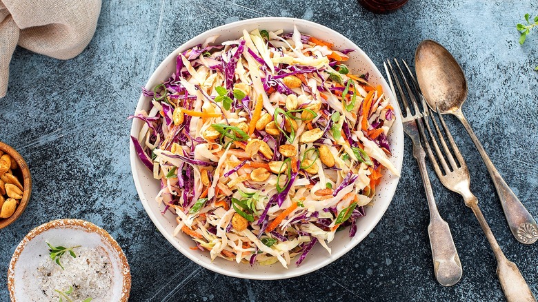 Top-down view of coleslaw mix with sliced green onions and halved peanuts in a white bowl