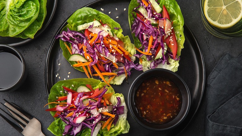 Asian-inspired coleslaw on romaine lettuce leaves topped with sesame seeds and served with a side of sweet Thai chili sauce