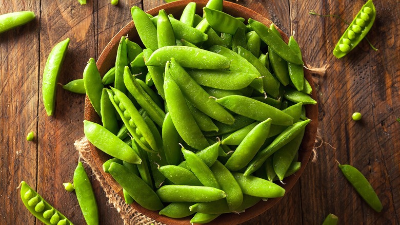Sugar snap peas in a wooden bowl on a small piece of burlap on a wooden surface
