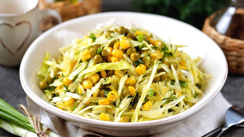 Coleslaw with yellow corn and capers in a shallow, white bowl