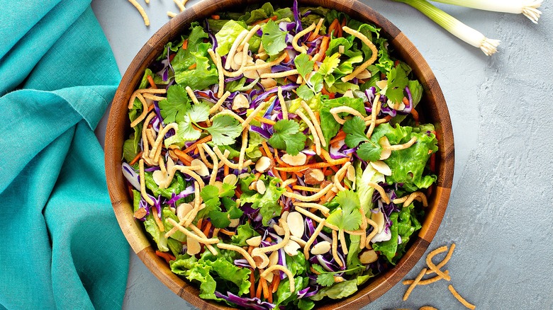 Asian-style slaw with cabbage, carrot, cilantro, crispy noodles, and sliced almonds in a wooden bowl