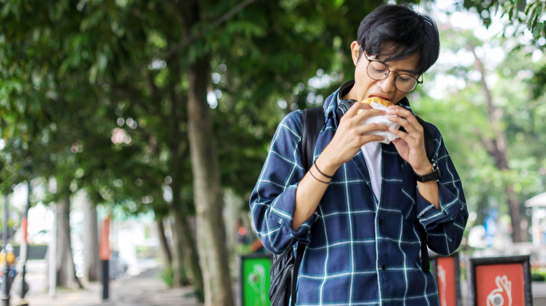 college student with glasses eating fast food burger