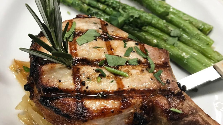 Bone-in grilled pork chop topped with garnish and served with asparagus