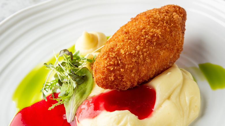 Fried chicken Kiev cutlet on mashed potatoes with sauce on white plate.