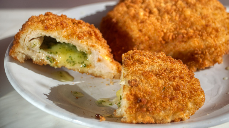 Whole chicken kiev cutlet plus one sliced with interior seasoned butter oozing out on plate.
