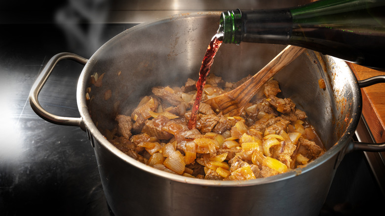Wine being poured into a pot of cooking stew