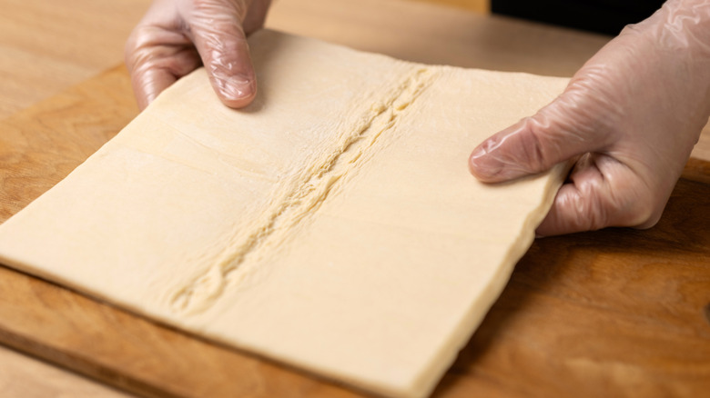 Hands holding frozen puff pastry sheet.