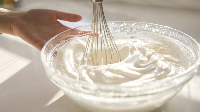 Whipping fresh meringue by hand in a glass bowl with a metal whisk