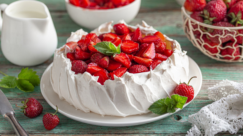 A pavlova on a white plate topped with fresh strawberries and mint