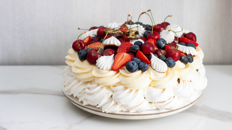 A composed pavlova with piped cream topped with fruit and chocolate