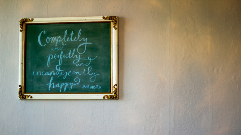 A gold-framed chalkboard is mounted on a wall that features a Jane Austen quote.