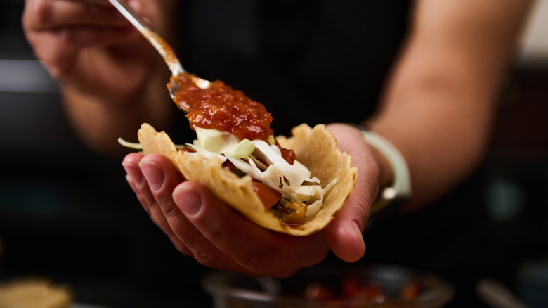 A hand adding a spoonful of salsa to tacos