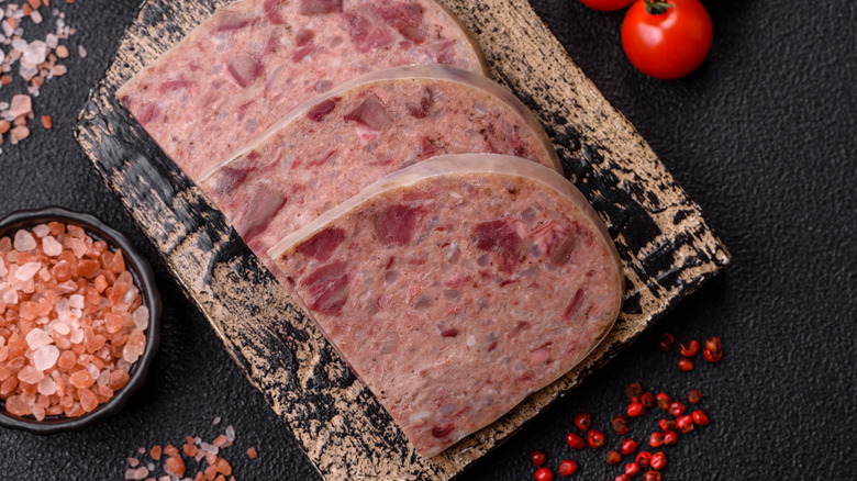 Homemade headcheese with salt, spices, herbs, and vegetables on a cutting board on a dark background