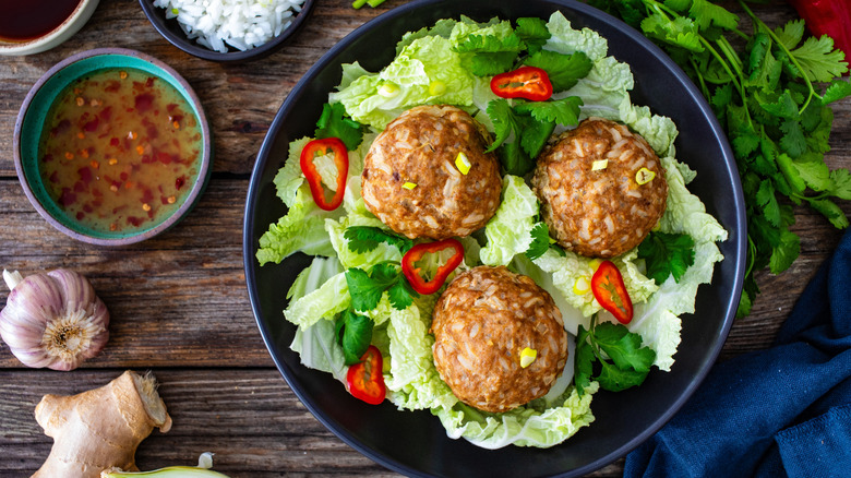 Lion's head meatballs served with vegetables in a bowl on a wooden table with a dish of dipping sauce next to it