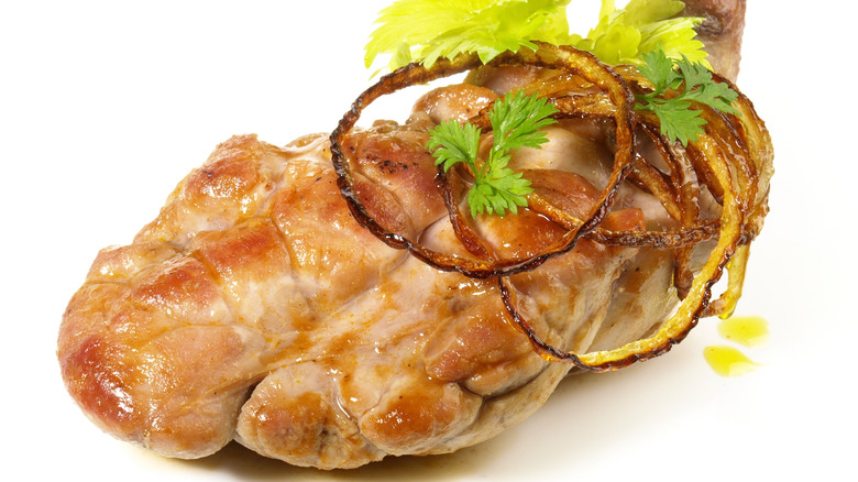 A roasted veal sweetbread with thin-cut onion rings on a white background