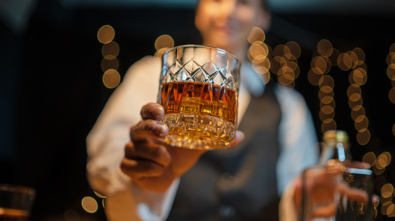 blurry waiter holding a glass of whisky, which is in focus