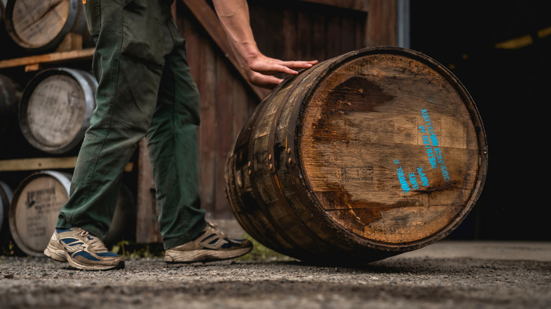 A person touching a whiskey barrel at a distillery